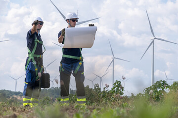 Workers discussing plans at a wind farm site with wind turbines in the background under a cloudy sky