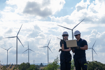 Engineers monitor wind turbine performance at renewable energy site during sunny day with clouds in background