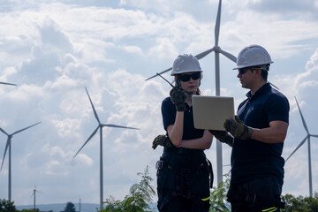 Workers discuss project details at a wind farm while looking at a tablet on a sunny day with wind turbines in the background