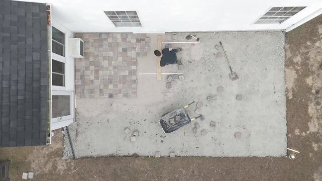 Overhead drone shots of man working on his backyard paver patio doing a DIY construction project. 