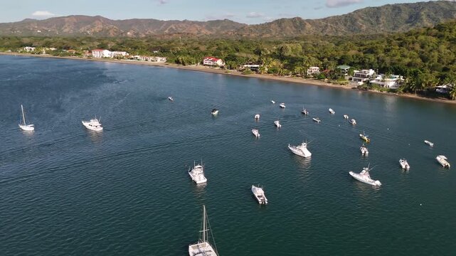 Fast aerial spin of recreation boats anchored off a Sandy beach overlooking beachfront condos and lush rainforest in Potrero Costa Rica Guanacaste,