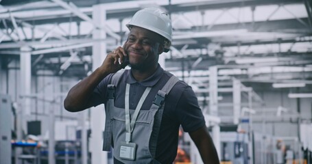 Industrial Male Engineer Walks Through High Tech Factory Floor While Talking on Smartphone and Smiling, Discussing With Colleague. Concepts Smart Manufacturing, Remote Coordination, and Industry 4.0.