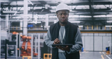 Engineer With Hard Hat Checking Data on Tablet. Male Engineer Provides Factory Inspection. Man Walks in Large, Modern Industrial Factory. Concept Mobile Management, Safety, and Operational Oversight.
