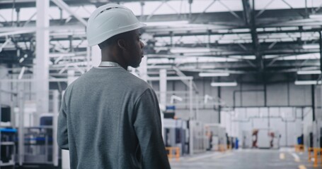 African American Adult Professional Engineer Walks at Head of Vast, Clean Automated Plant, Wearing Hard Hat. Concept of Physical Presence and Direct Control Over Complex Modern Robotic Systems.