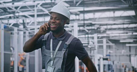Industrial Male Engineer Walks Through High Tech Factory Floor While Talking on Smartphone and Smiling, Discussing With Colleague. Concepts Smart Manufacturing, Remote Coordination, and Industry 4.0.