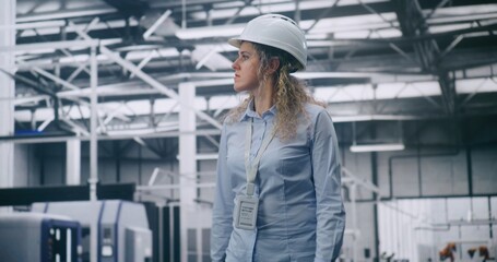 Curly Haired Woman Wearing Protective Helmet Moves Calmly Across High Tech Factory Floor, Observing Robotic Systems and Automated Machinery in Operation. Concept of Digital Manufacturing, Innovation.
