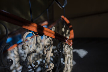 Close-up of Ornate Wrought-Iron and Wood Staircase Railing. Dramatically Sunlit Vintage interior.