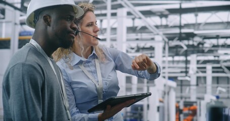 Two Specialists Solve Technical Issue in Vast Industrial Plant. Woman Points Area Concern on Factory Floor, Using Tablet For Data Reference. Problem Solving and Operational Excellence in Industry 4.0.