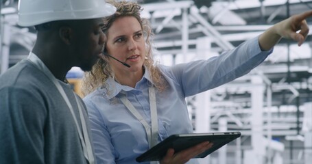 Technical Team Performing on Site Inspection in Modern Automated Factory. Female Manager Uses Tablet Review Digital Schematics While Guiding Male Engineer. Mobile Technology Integration in Industrial
