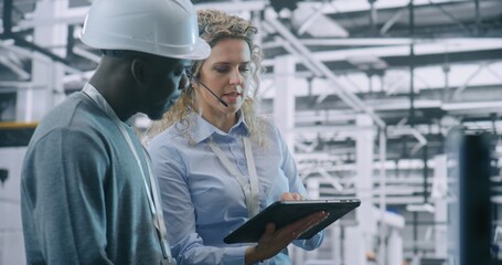 Two Specialists Solve Technical Issue in Vast Industrial Plant. Woman Points Area Concern on Factory Floor, Using Tablet For Data Reference. Problem Solving and Operational Excellence in Industry 4.0.