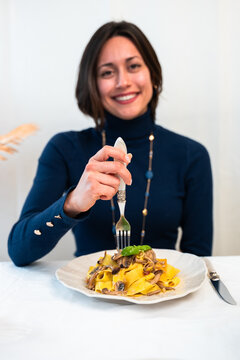 Smiling woman eating homemade tagliatelle pasta with mushrooms at home