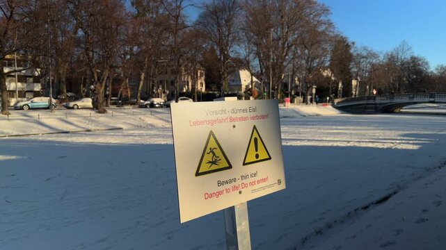 Safety notice in Neuhausen-Nymphenburg, Munich. A sign warns of dangerous thin ice and life hazard on the frozen canal. Ideal for winter safety, urban park, and German travel themes.