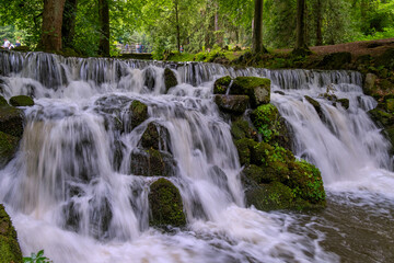 Tranquil Waterfall With Lush Surroundings, Serene Waterfall Flowing Beneath Stone Bridge Amidst Vibrant Woods