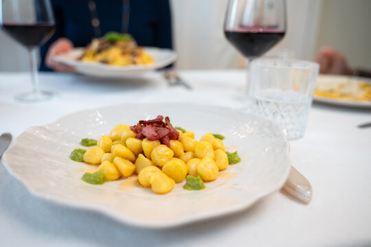 Gnocchi with bacon and green sauce served with red wine on dining table