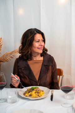 Smiling woman enjoying homemade pasta and red wine at cozy dinner table