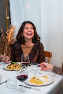Vertical portrait of smiling woman enjoying homemade pasta and red wine at cozy dinner