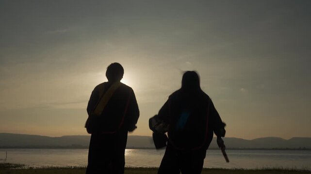 Silhouette of two graduates throwing diplomas in the air at sunset, celebrating success, freedom, and the end of their academic journey.