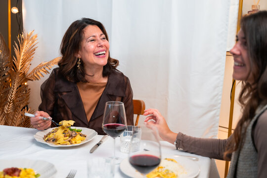 Vertical lifestyle photo of joyful mature woman laughing during Italian pasta dinner with friends