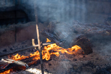 Smoky traditional asado meat roasting over an open wood fire