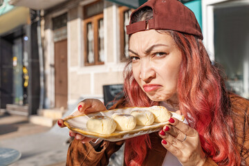 Young woman looking with a face of disgust while holding a plate of traditional sweets on a city street