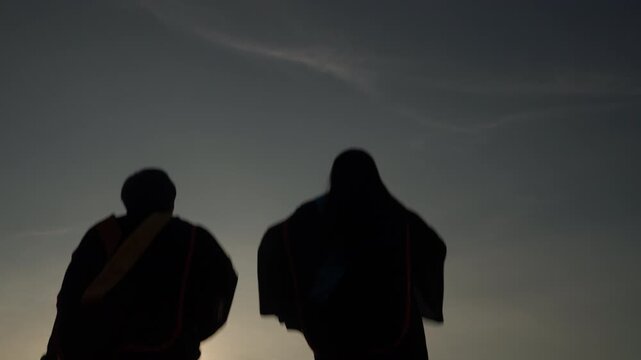 Silhouette of joyful graduates raising diploma and graduation cap into the air at dusk, expressing freedom, celebration, and academic success.