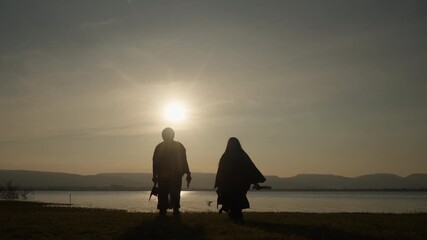 Silhouette of two graduates throwing hats and holding diplomas by the lake during sunset, symbolizing freedom, celebration, and academic success.