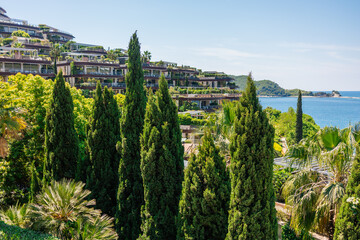 Modern resort buildings surrounded by lush greenery near the sea. Mediterranean Montenegro coastal lifestyle, luxury hospitality, summer vacation atmosphere and architectural harmony with natural