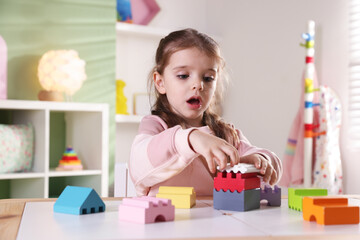 Little girl playing with toys at white table in playroom
