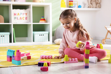 Fototapeta premium Little girl playing with toys on floor in playroom