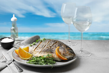 Delicious cooked fish with oranges served on grey table at beach. Sea food