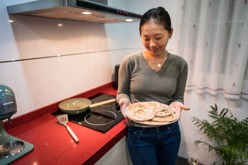 Woman presenting freshly made pita bread in kitchen