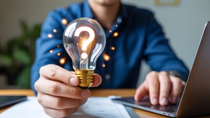 Person Holding a Light Bulb with a Question Mark Symbol in Front of a Laptop on a Desk with Documents