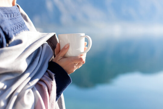 Cup of morning coffee in hands outdoors in nature. Woman drinking hot beverage, relaxing by mountain lake. Cozy winter coolcation. Traveler enjoying healthy fancy non alcoholic drink, dry January