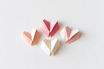 A collection of four beautifully crafted origami hearts in shades of pink and cream, showcasing intricate folding techniques on a light background.