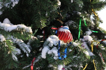 a green Christmas tree in the snow, decorated with a red ball and tinsel