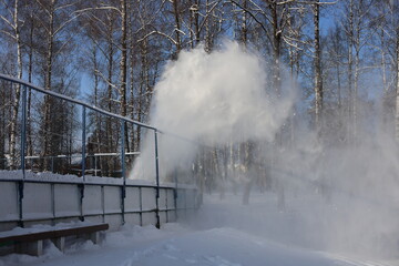 A snowplow scatters snow into the air on a skating rink