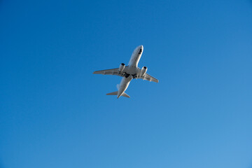 Obraz premium White Commercial Airplane Ascending into Clear Blue Sky Right After Airport Takeoff. White Passenger Plane Soaring Through Sunny Blue Sky – Air Travel and Vacation Concept