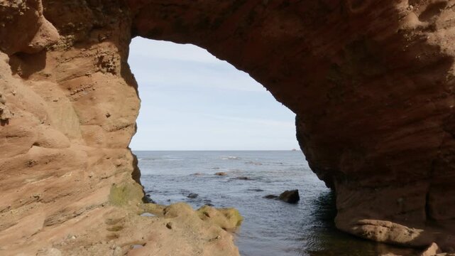 Through a natural arch in Aberdour beach area in Scotland.