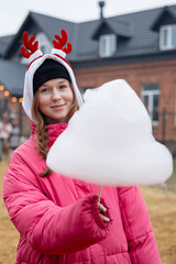 Teen girl in a pink winter jacket holding large cotton candy at an outdoor fair.