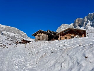 Charming wooden huts surrounded by snow in Partnun, with Sulzfluh and Scheienfluh in the background. Partner, Graubuenden, Switzerland.