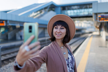 beautiful tourist girl takes a selfie at the station. A girl in a hat and coat at the station.