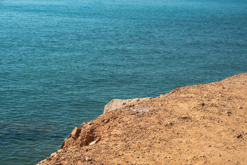 View of a soil cliff and ground erosion at the edge of the blue sea. Environmental change and coastal geography.