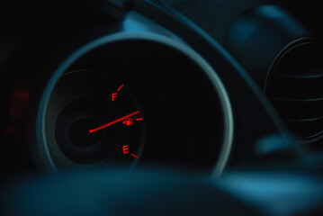 Car fuel gauge showing fuel level with red warning light illuminated on a dark dashboard. Concept of fuel consumption and transportation safety.