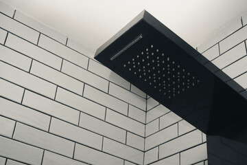 Close up of a sleek modern black rain shower head mounted on a white brick tile wall in a contemporary bathroom.