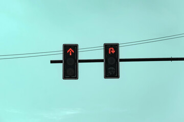 Red traffic light showing straight arrow and u-turn signal against a teal sky background. Traffic control and road safety.