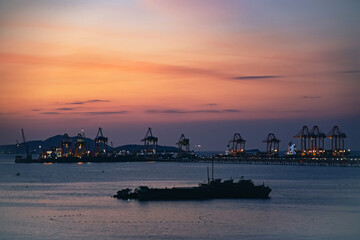View of a commercial shipping port with container stacks and industrial cranes at sunset. Global import export and supply chain industry.