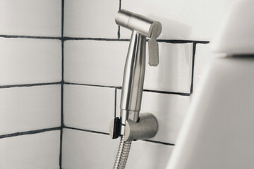 Stainless steel handheld bidet spray on white tiled bathroom wall. Concept of hygiene, sanitation, modern bathroom, plumbing, and clean lifestyle.