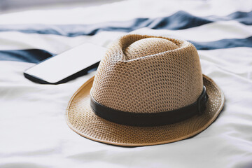 Straw fedora hat and a smartphone placed on a striped bed sheet. Travel planning, vacation, and relaxation concept.