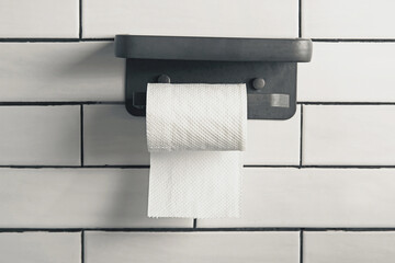 Toilet tissue paper roll mounted on a holder against white tile wall. Minimal home bathroom interior. Concept for hygiene, cleanliness and restroom