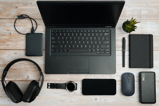Flat lay business workspace with laptop, smartphone, headphones, mouse, notebook, watch, and accessories on white wooden desk representing productivity, and digital professional lifestyle. - Powered by Adobe